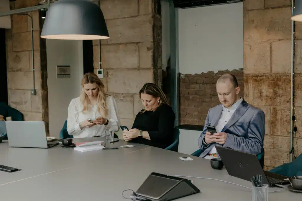 Three people sitting around a conference table on their phones